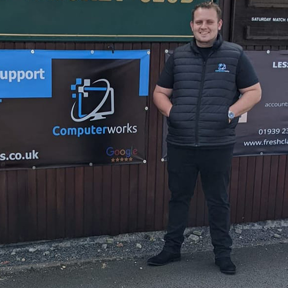 Computerworks representative standing proudly beside the company's sponsorship advertising board at Wem Cricket Club, showcasing support for the local community.
